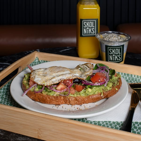 Avocado toast with fried egg, tomatoes, red onion, and spinach, served with Skol Niks juice and chia pudding.