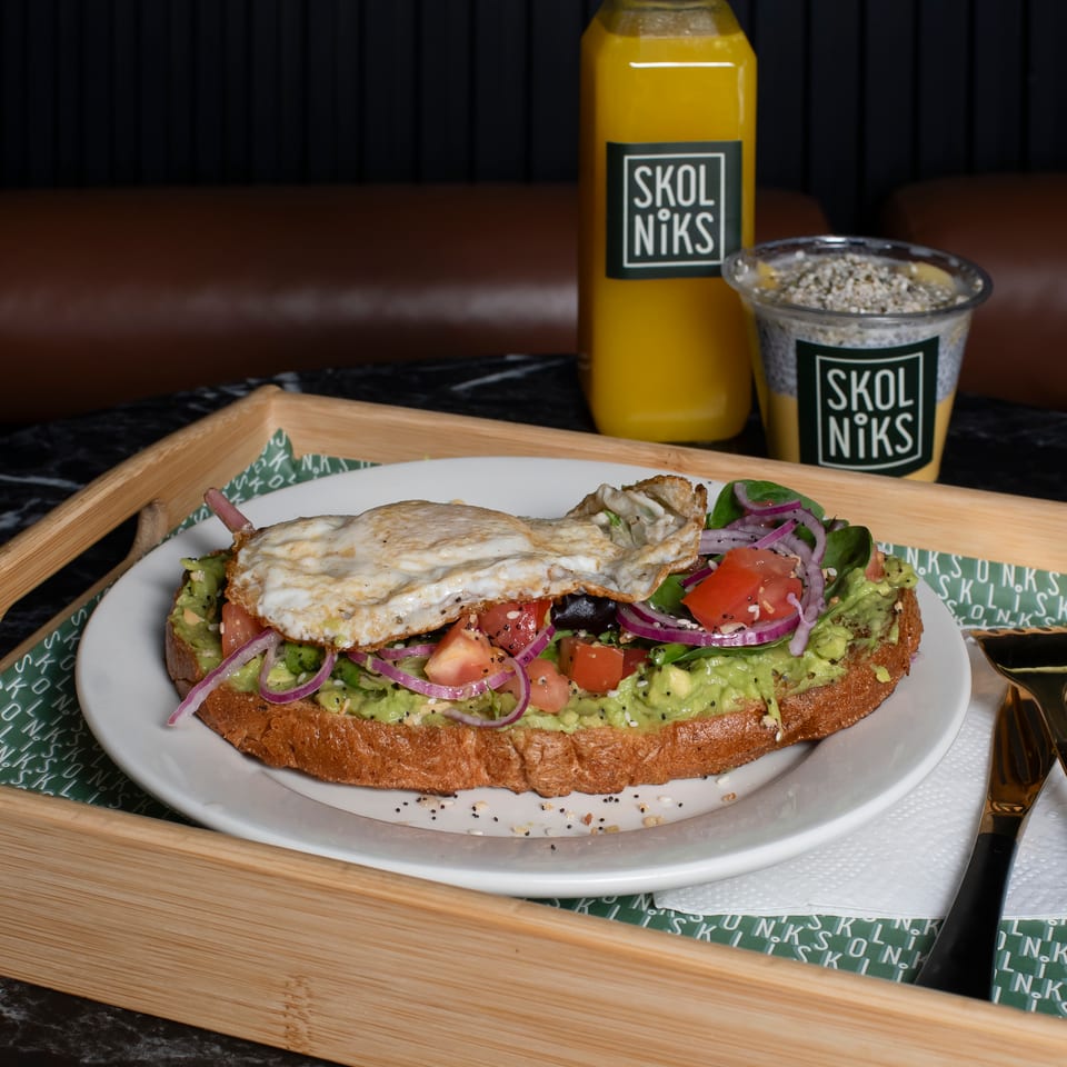 Avocado toast with fried egg, tomatoes, red onion, and spinach, served with Skol Niks juice and chia pudding.