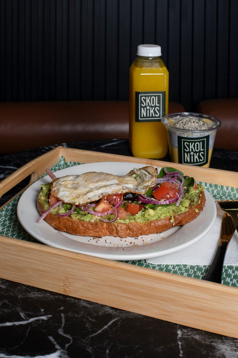 Avocado toast with fried egg, tomatoes, red onion, and spinach, served with Skol Niks juice and chia pudding.