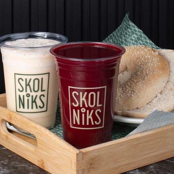 Two Skol Niks branded drinks, one white and one red, with sliced bagels on a wooden tray.