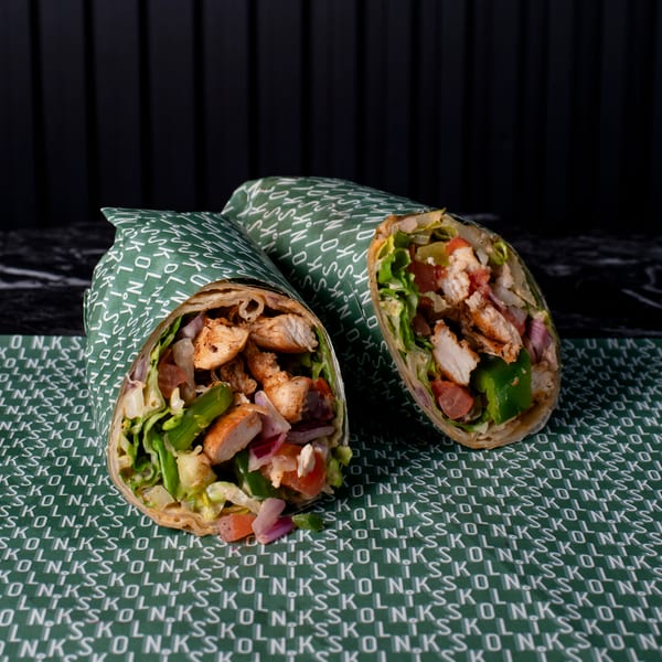 Two chicken wraps, filled with lettuce, tomatoes, and onions, on green branded paper.