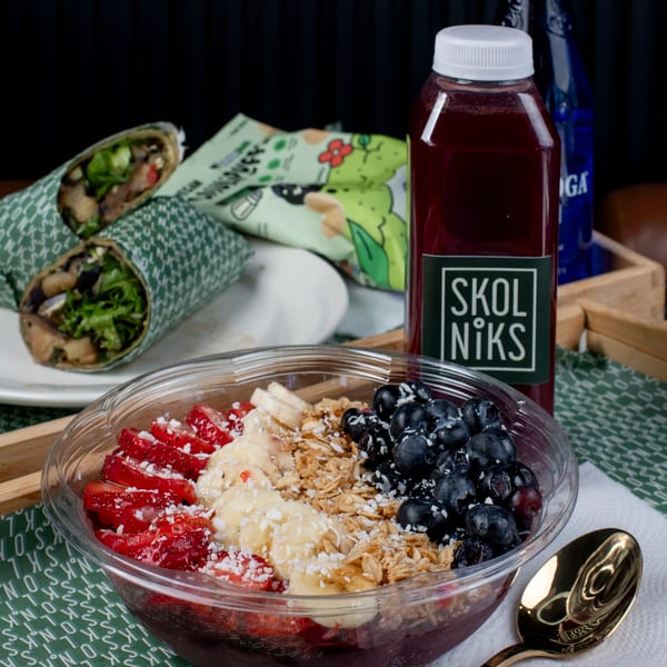 A Skolniks acai bowl with strawberries, bananas, blueberries, and granola, next to wraps and drinks.